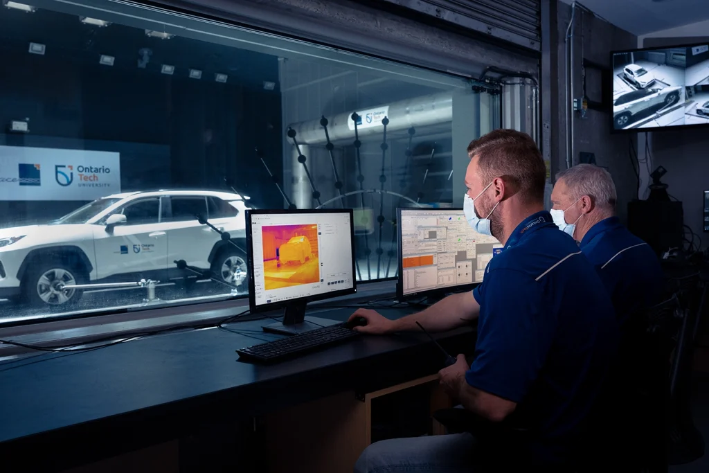 Two guys sitting in a booth looking at computers analyzing a white toyota car in the shop